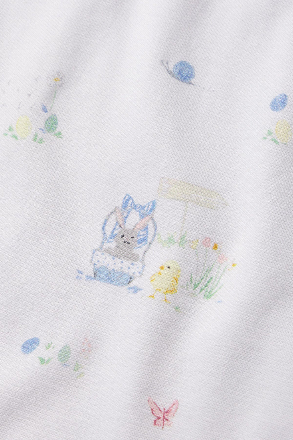 A close-up of the Kids Long-Long Set in Easter Egg Hunt, featuring white Pima cotton with a pastel bunny wearing a blue bow in a basket beside a yellow chick, surrounded by flowers, grass, and colorful Easter eggs.
