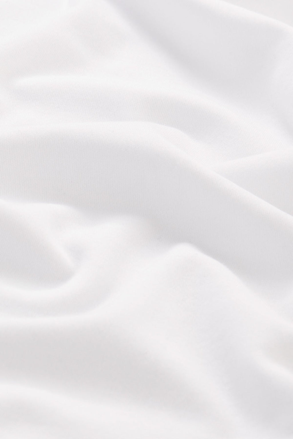 Close-up of the Pima Scallop Robe in White, showcasing its luxurious 100% Pima cotton fabric with smooth folds and a gentle texture. The light material is slightly draped, creating subtle shadows and highlights on its surface.
